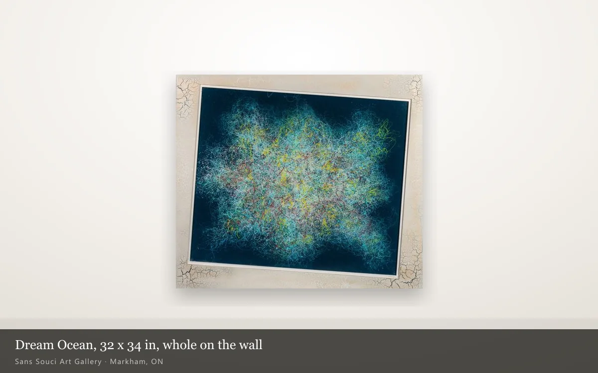 Dream Ocean shown whole on a pale gallery wall: a dark navy field with a cloud of turquoise and yellow threads, inside a wide cream border with crackle at the corners