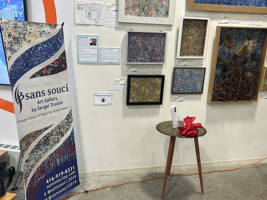 The Sans Souci Art Gallery banner beside framed paintings and a small round table holding cards and a red bow
