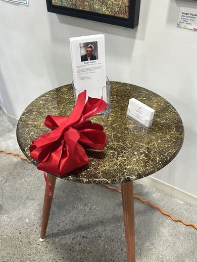 Round marbled side table with a stand of the artist's cards and a red bow